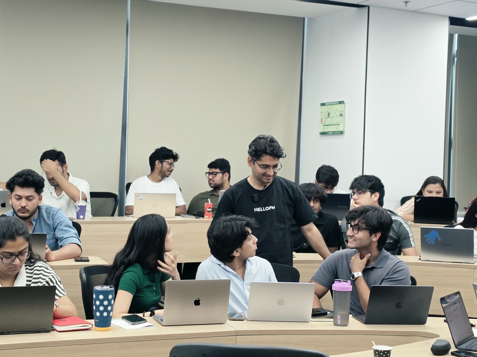 A HelloPM host talking with attendees working on laptops at a masterclass