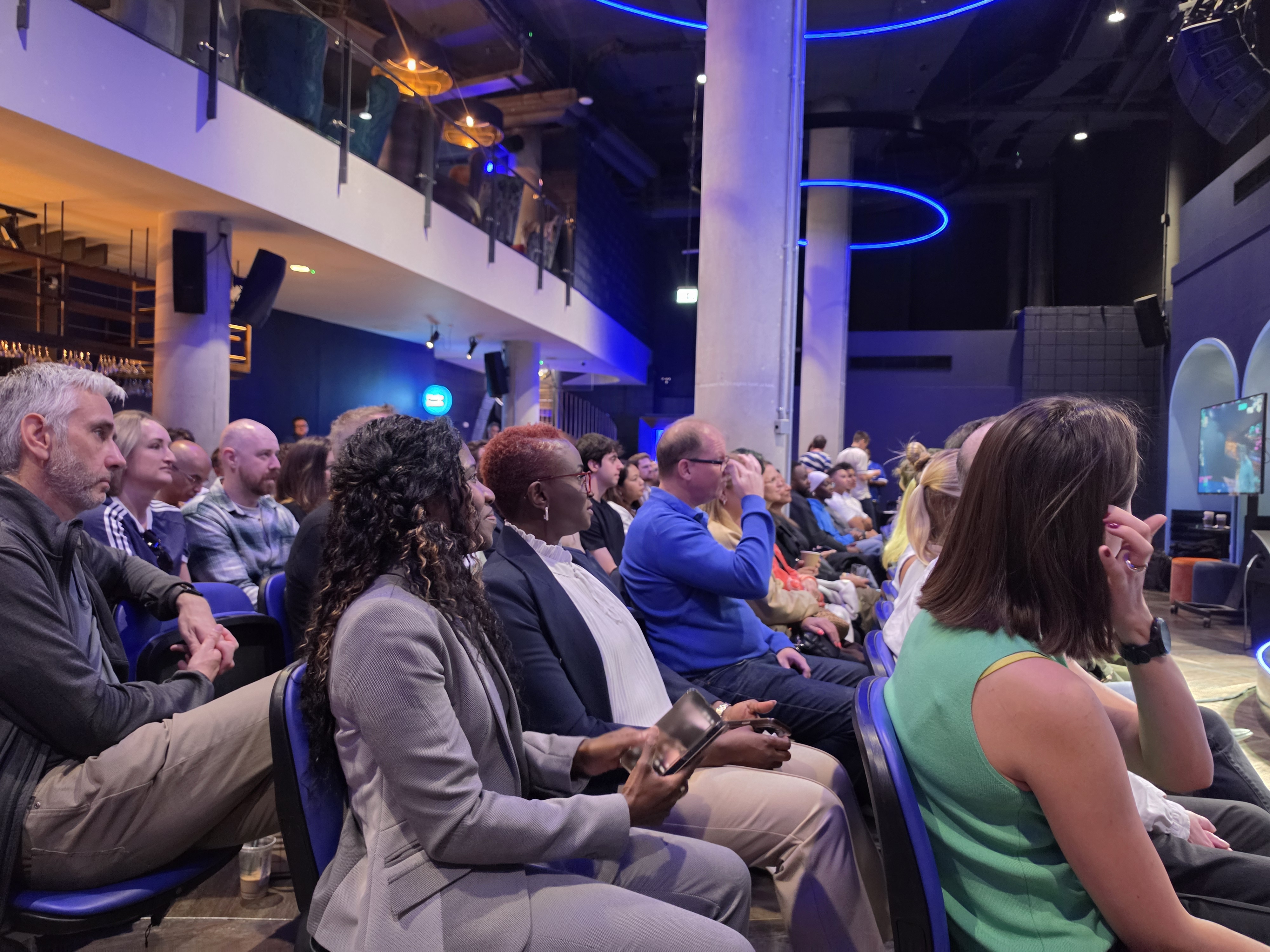 Attentive audience seated at a HelloPM London event under blue lighting