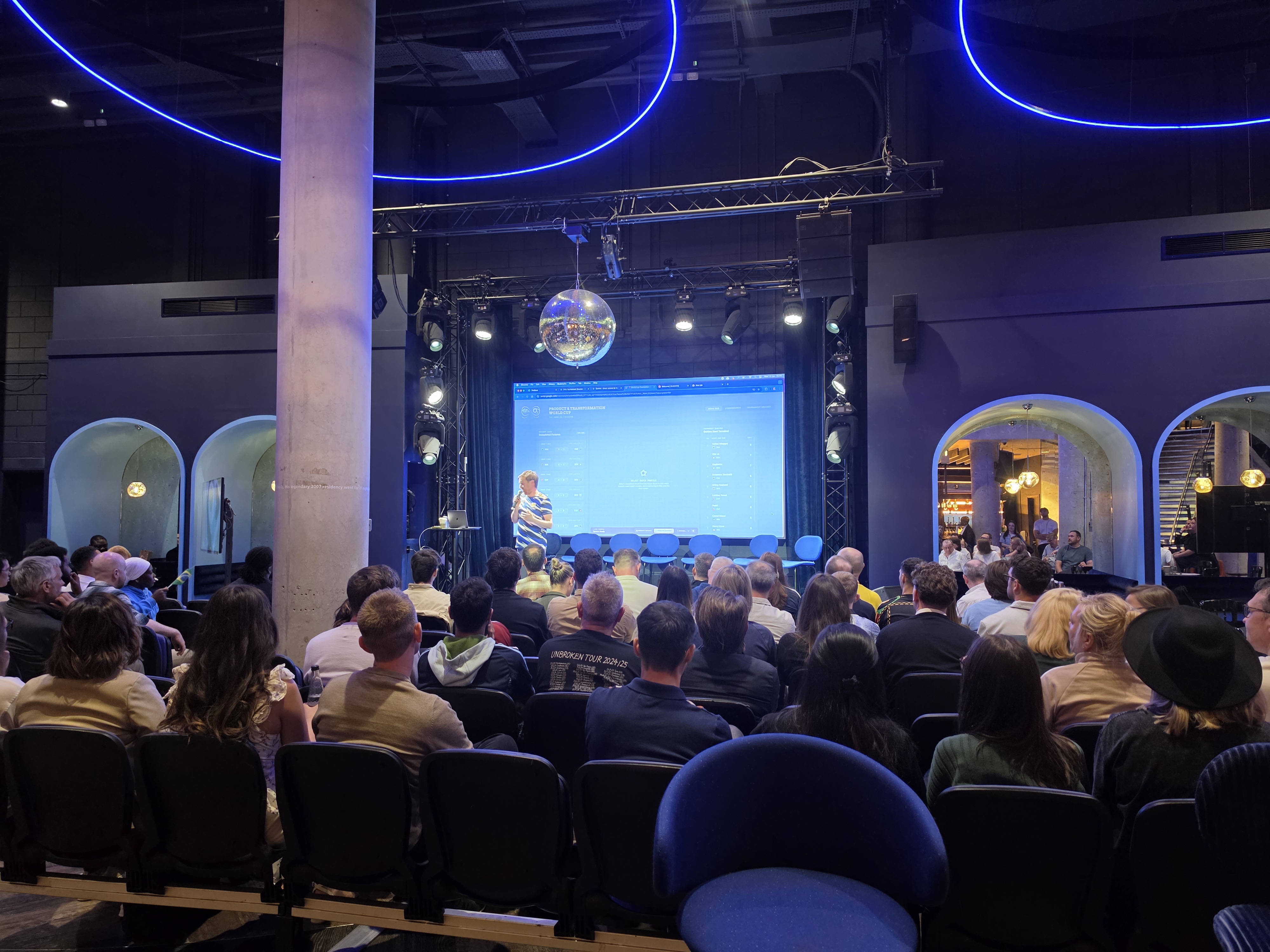 Wide view of the HelloPM London venue with a stage and audience